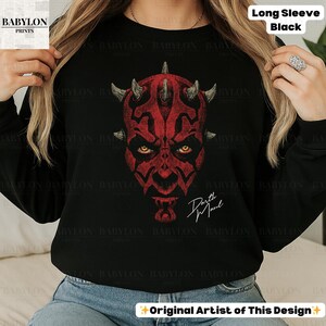 Może przedstawiać: Czarna koszulka z długim rękawem z czerwoną grafiką Darth Maul. Projekt przedstawia twarz postaci z rogami i imieniem "Darth Maul" w białym skrypcie. Koszulka ma napis "Long Sleeve Black" w prawym g&oacute;rnym rogu.