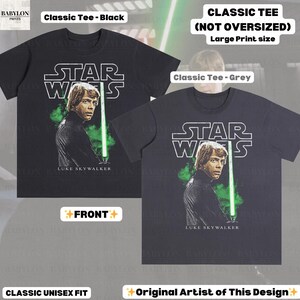 May include: Black and grey classic unisex fit t-shirts featuring a large print of Luke Skywalker with a green lightsaber and the Star Wars logo. The text "LUKE SKYWALKER" is below the image. The shirts are labeled "Classic Tee" and "Original Artist of This Design."