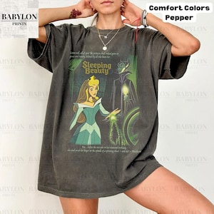 May include: Dark grey t-shirt featuring a Sleeping Beauty graphic. The design includes an illustration of Aurora and Maleficent, with text from the story. The shirt is from Babylon Prints and is part of the Comfort Colors collection.