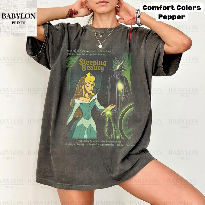 May include: Dark grey t-shirt featuring a Sleeping Beauty graphic. The design includes an illustration of Aurora and Maleficent, with text from the story. The shirt is from Babylon Prints and is part of the Comfort Colors collection.