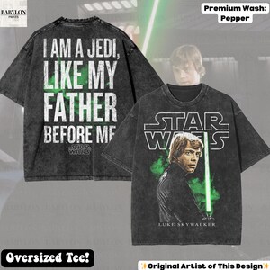 May include: A dark gray oversized t-shirt featuring Luke Skywalker with a green lightsaber and the Star Wars logo. The back of the shirt displays the text "I AM A JEDI, LIKE MY FATHER BEFORE ME."