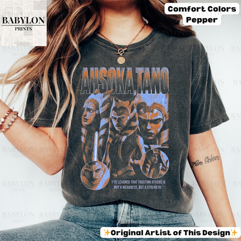 May include: A black t-shirt with a faded graphic of Ahsoka Tano from Star Wars. The graphic is in blue and orange and features a quote from the show: "I've learned that trusting others is not a weakness, but a strength."
