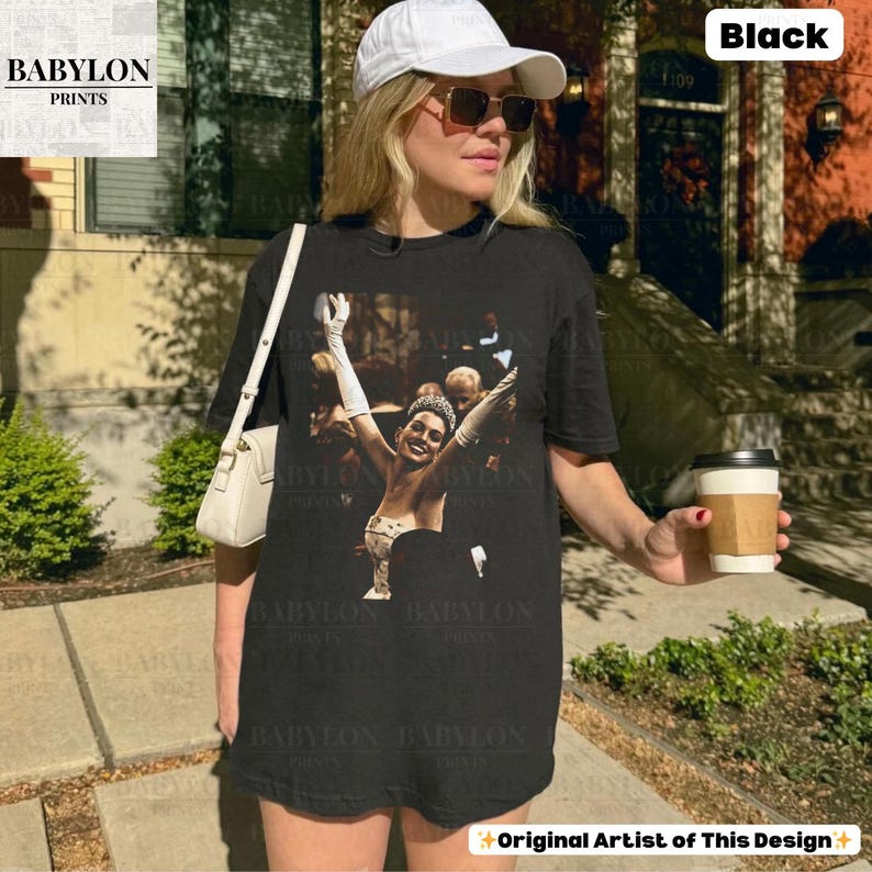 May include: Black t-shirt with a vintage image of a woman in a gown with her arms raised. The shirt has the text "BABYLON PRINTS" and "Original Artist of This Design". The model is wearing a white cap and sunglasses.