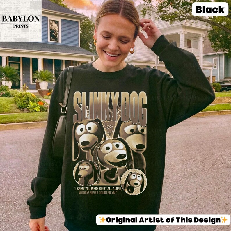 May include: Black sweatshirt featuring a graphic of Slinky Dog from Toy Story. The design includes the text "SLINKY DOG" and the quote "I KNEW YOU WERE RIGHT ALL ALONG, WOODY! NEVER DOUBTED YA!" The sweatshirt has long sleeves and a crew neck.