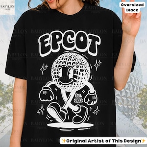 Pu&ograve; includere: T-shirt nero oversize con grafica bianca di un personaggio sferico geometrico sorridente e la scritta "EPCOT". La grafica include il testo "Est. 1982". La maglietta ha la scritta "Original Artist of This Design".
