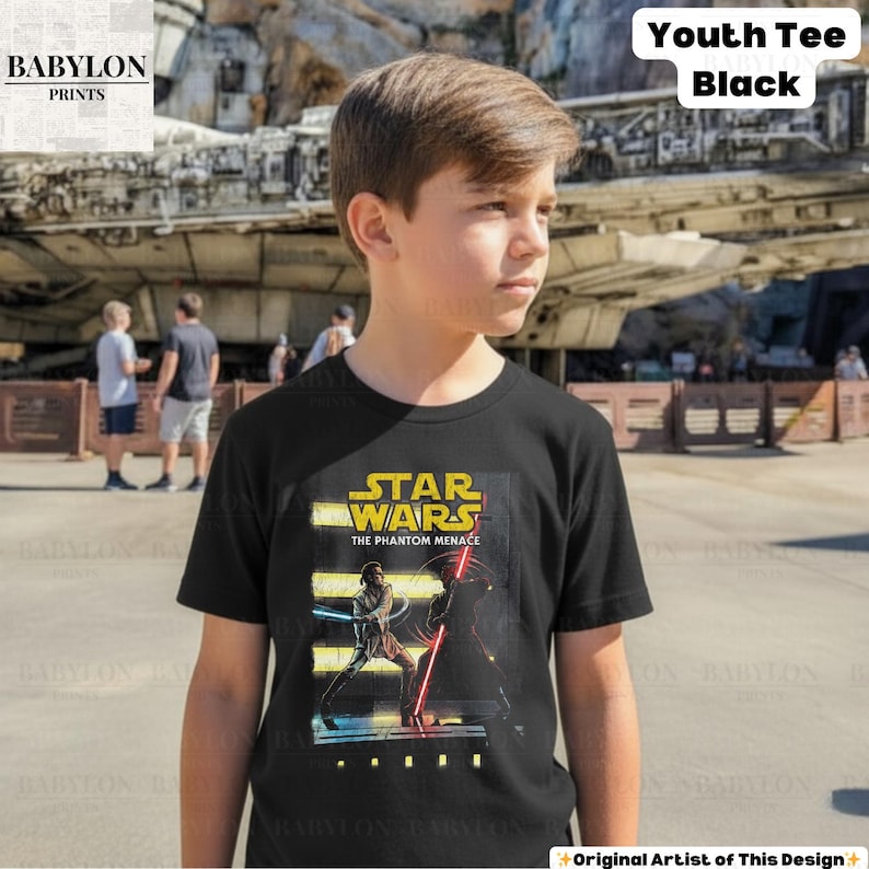 Puede incluir: Camiseta negra juvenil con un gr&aacute;fico de Star Wars: La Amenaza Fantasma. El dise&ntilde;o incluye el t&iacute;tulo de la pel&iacute;cula y personajes con sables de luz. La camiseta est&aacute; etiquetada como "Youth Tee Black" y es de Babylon Prints.