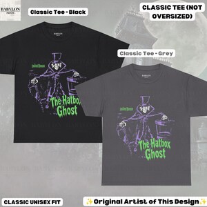 Puede incluir: Una camiseta negra y una gris de manga corta, cada una con un estampado gr&aacute;fico de The Hatbox Ghost de la Haunted Mansion. El dise&ntilde;o incluye al personaje con sombrero de copa sosteniendo una sombrerera, con el texto en verde.