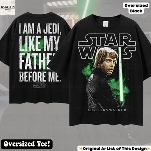 May include: Black oversized t-shirt featuring Luke Skywalker from Star Wars. The front displays Luke with a green lightsaber and the Star Wars logo. The back has the text "I AM A JEDI, LIKE MY FATHE BEFORE ME." A perfect gift for Star Wars fans.