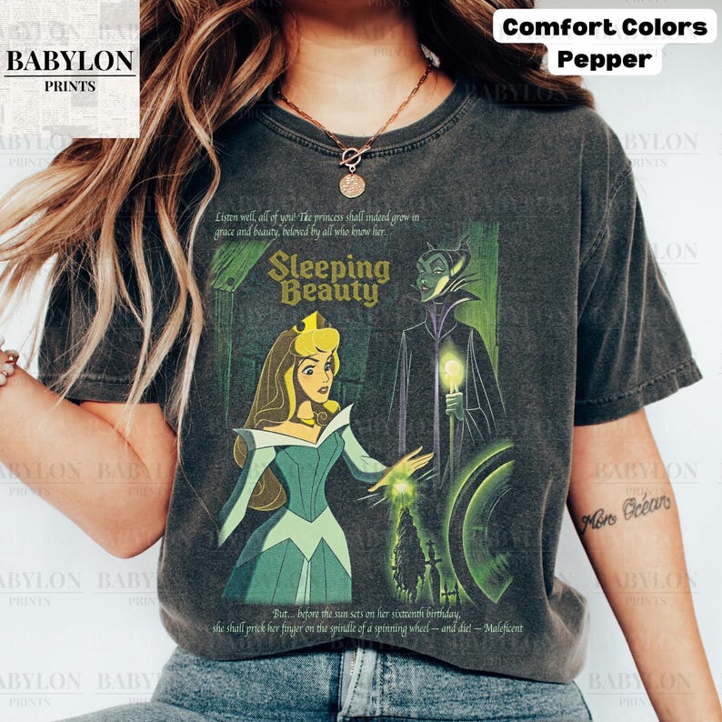 May include: Dark gray t-shirt featuring a graphic from the Disney movie Sleeping Beauty. The design includes Princess Aurora and Maleficent, with text from the film. The shirt is labeled "Comfort Colors" and "Pepper".