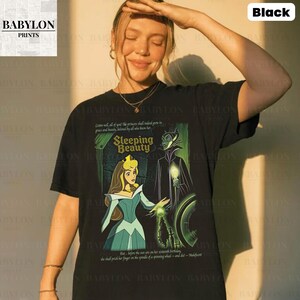 May include: Black t-shirt featuring a Sleeping Beauty graphic. The design includes Princess Aurora and Maleficent, with text from the movie. The shirt is a classic crew neck style.
