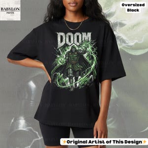 May include: Black oversized t-shirt featuring the word "DOOM" in a bold, stylized font above a graphic of a character in a green and black outfit with green energy effects. The shirt is from Babylon Prints.