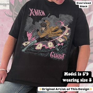 May include: Black oversized t-shirt featuring a graphic of the X-Men character Gambit. The design includes the character wielding a staff and playing cards. The shirt has the words "X-MEN" and "GAMBIT" printed on it.