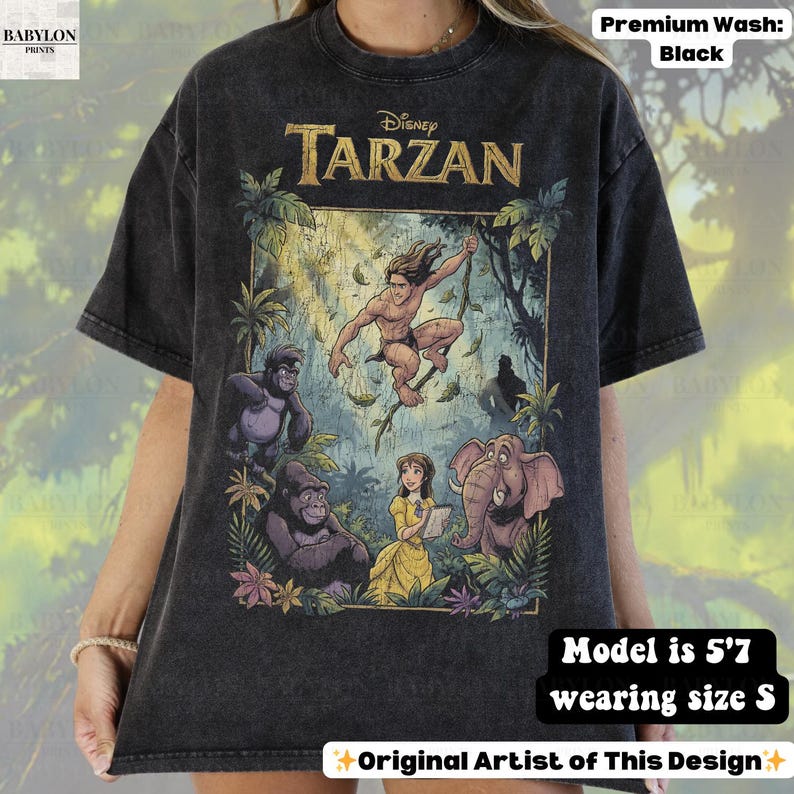 May include: Black, short-sleeved t-shirt featuring a graphic of Disney's Tarzan. The design includes Tarzan, gorillas, Jane, and an elephant in a jungle setting. The shirt has the text "Disney Tarzan" at the top. The model is 5'7" and wearing size S.