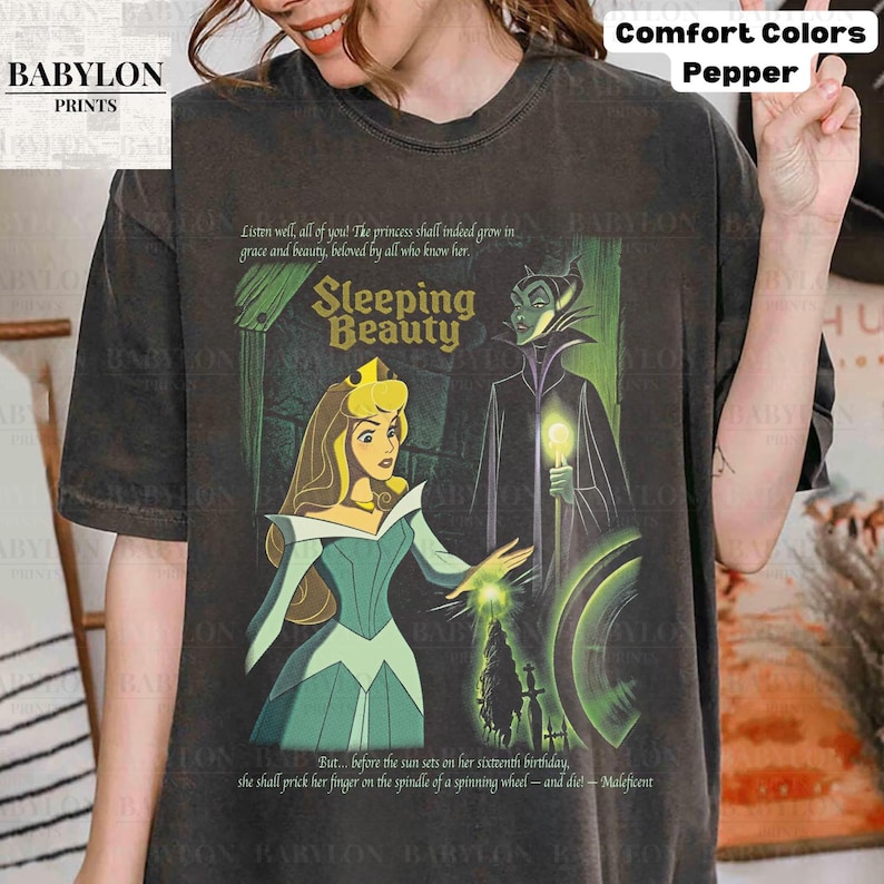 May include: Dark gray t-shirt featuring a Sleeping Beauty graphic. The design includes Princess Aurora, Maleficent, and text from the movie. The shirt is from Comfort Colors and has the Babylon Prints logo.