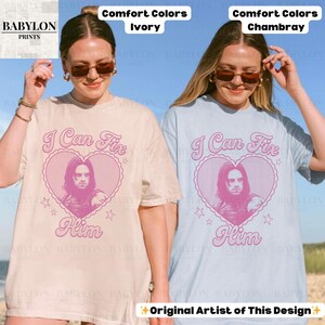 May include: Two t-shirts, one ivory and one chambray, each with a pink heart design featuring a portrait and the text "I Can Fix Him." The design includes stars and the words "Him." The shirts are from Babylon Prints.