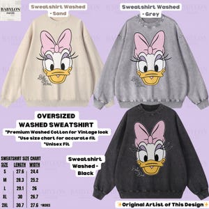Puede incluir: Sudaderas lavadas de gran tama&ntilde;o en arena, gris y negro, cada una con un gr&aacute;fico de Daisy Duck con un lazo rosa. La imagen incluye una tabla de tallas. Las sudaderas est&aacute;n hechas de algod&oacute;n lavado de primera calidad para un aspecto vintage.