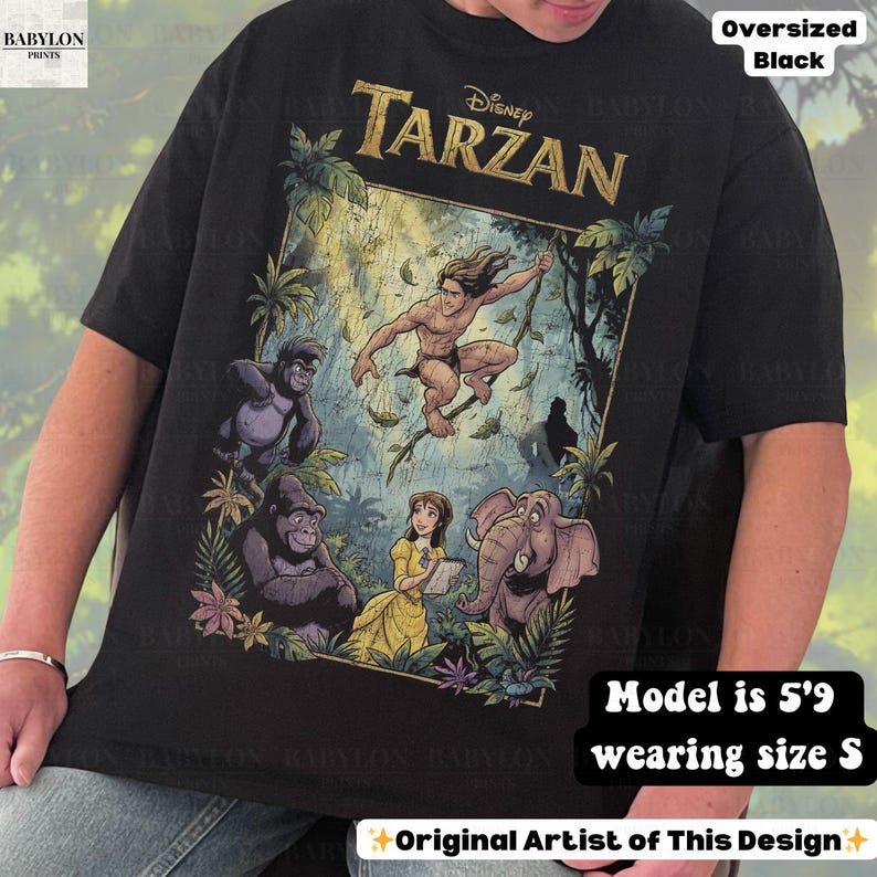 May include: Black oversized t-shirt featuring a colorful graphic of Disney's Tarzan. The design includes Tarzan, gorillas, Jane, and an elephant. The shirt has the text "Disney Tarzan" in gold lettering. The text "Original Artist of This Design" is also visible.