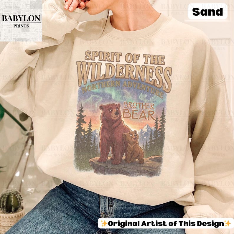 May include: Sand-coloured sweatshirt with a graphic of two bears and the text "Spirit of the Wilderness" and "Brother Bear." The design includes trees, mountains, and the text "Northern Adventure."