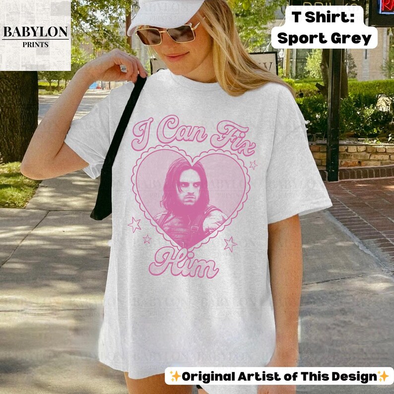 May include: White t-shirt with a pink heart graphic featuring a portrait and the text "I Can Fix Him." The shirt also has the text "Original Artist of This Design" and "T Shirt: Sport Grey."