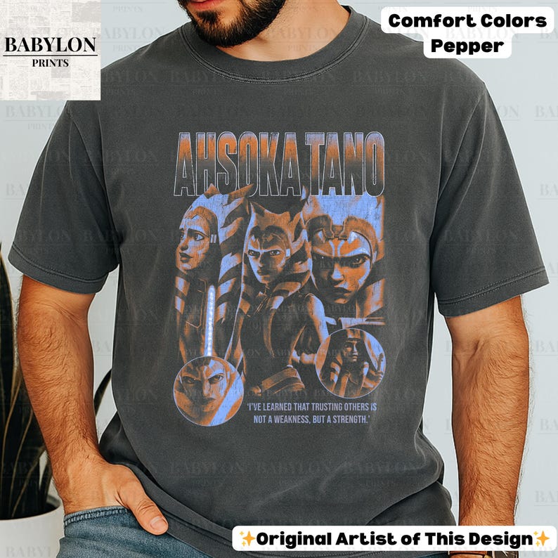 May include: A black t-shirt with a faded vintage look featuring a graphic of Ahsoka Tano from Star Wars. The graphic includes a quote from the show: "I've learned that trusting others is not a weakness, but a strength."