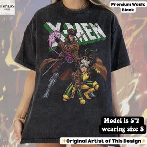 May include: Black t-shirt featuring the X-Men logo and comic book characters Gambit and Rogue. The shirt has a distressed look and the text "Original Artist of This Design". The model is 5'7" and wearing a size S.