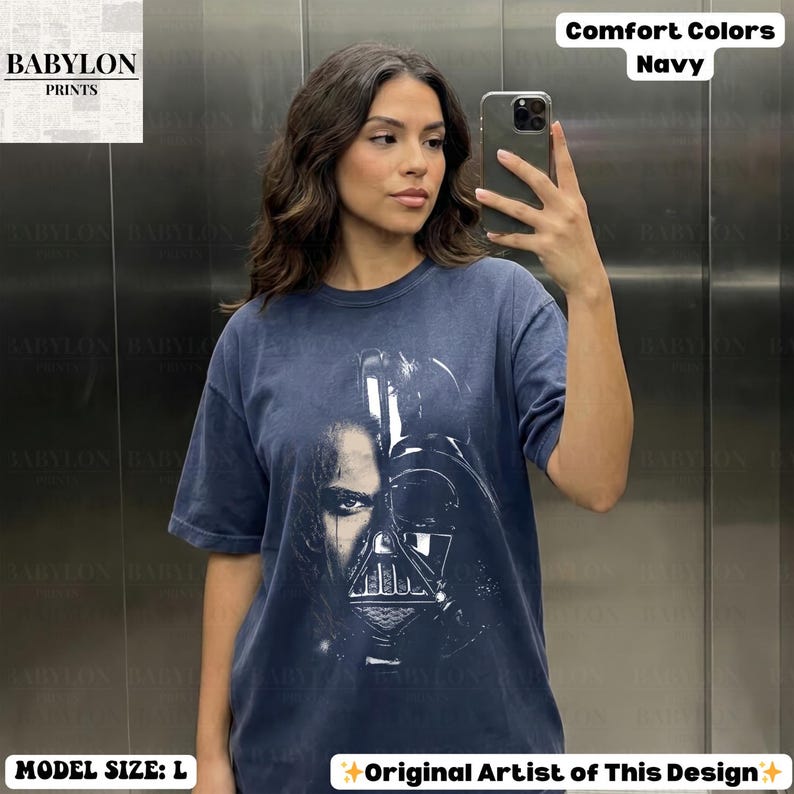 May include: Navy blue t-shirt featuring a graphic of Darth Vader. The shirt has the text "Comfort Colors Navy" and "Original Artist of This Design". The model is wearing a size L.