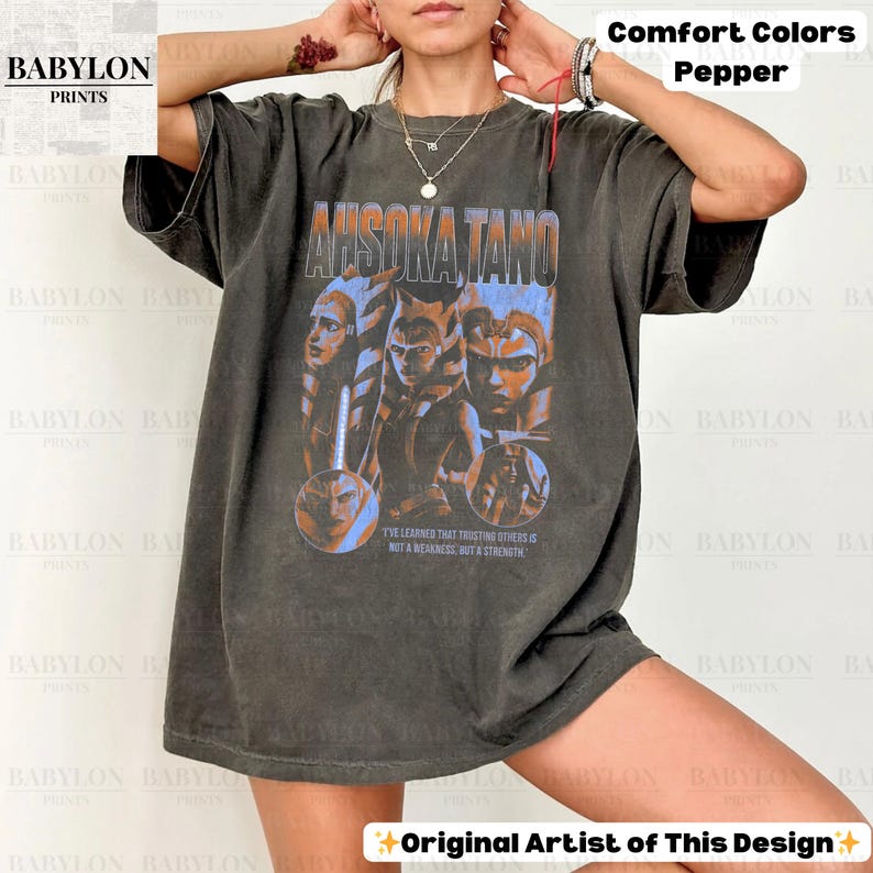 May include: A dark gray t-shirt with a faded graphic of Ahsoka Tano and the text "Ahsoka Tano" and "I've learned that trusting others is not a weakness, but a strength".