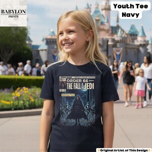 May include: A navy blue youth tee featuring a Star Wars comic book cover design. The graphic reads "Star Wars Special Variant Edition Order 66 The Fall of Jedi". The shirt is worn by a young person in front of a castle.