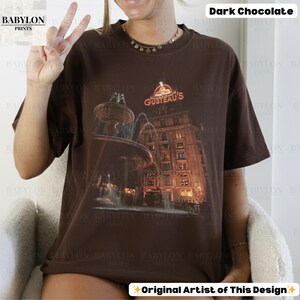 May include: A dark chocolate t-shirt with a graphic of a fountain and building, and the text "GUSTEAU'S". The shirt is from "BABYLON PRINTS" and is labeled "Original Artist of This Design".