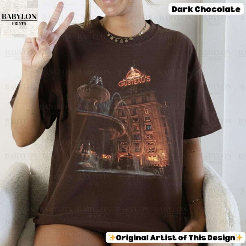 May include: A dark chocolate t-shirt with a graphic of a fountain and building, and the text "GUSTEAU'S". The shirt is from "BABYLON PRINTS" and is labeled "Original Artist of This Design".