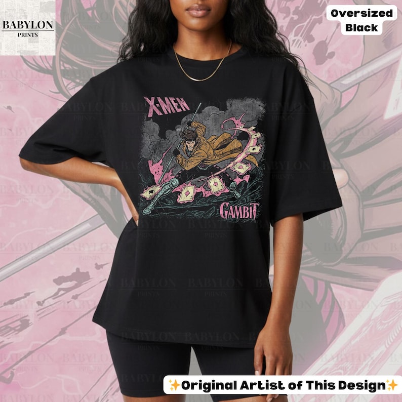 May include: Black oversized t-shirt featuring a graphic of the X-Men character Gambit. The design includes the text "X-Men" and "Gambit" in pink, along with an illustration of the character. The shirt is labeled "Oversized Black" and "Original Artist of This Design."
