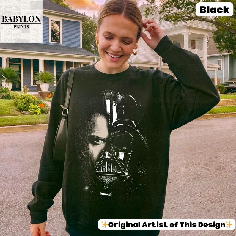 May include: Black sweatshirt featuring a graphic of Darth Vader's face. The sweatshirt has long sleeves and a crew neck. The text "Original Artist of This Design" is at the bottom. The Babylon Prints logo is in the upper left corner.
