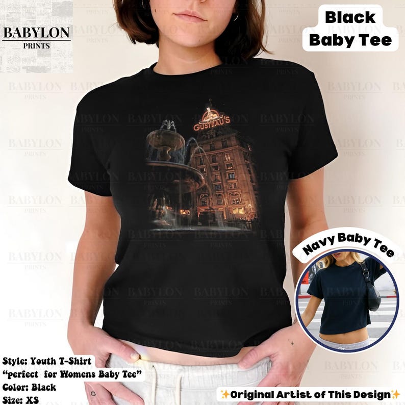May include: Black youth T-shirt with a graphic of a building and the text "GUSTEAU'S". The shirt also has the text "Black Baby Tee" printed on it. The shirt is size XS. The image also shows a "Navy Baby Tee".