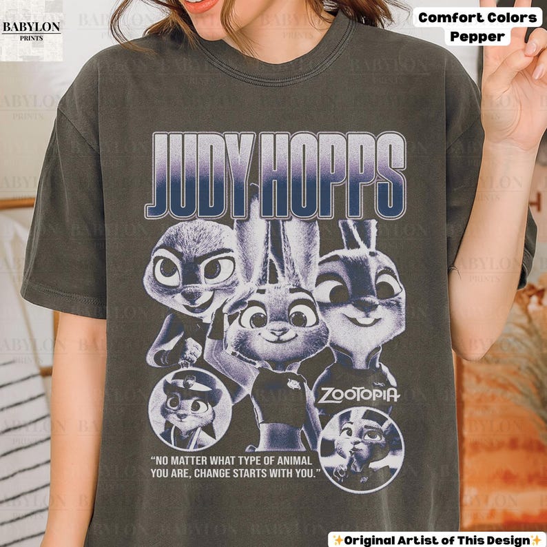 May include: Dark gray t-shirt featuring the text "JUDY HOPPS" in a gradient blue and white font, with images of the character Judy Hopps from the movie Zootopia. The shirt also includes the quote, "NO MATTER WHAT TYPE OF ANIMAL YOU ARE, CHANGE STARTS WITH YOU."
