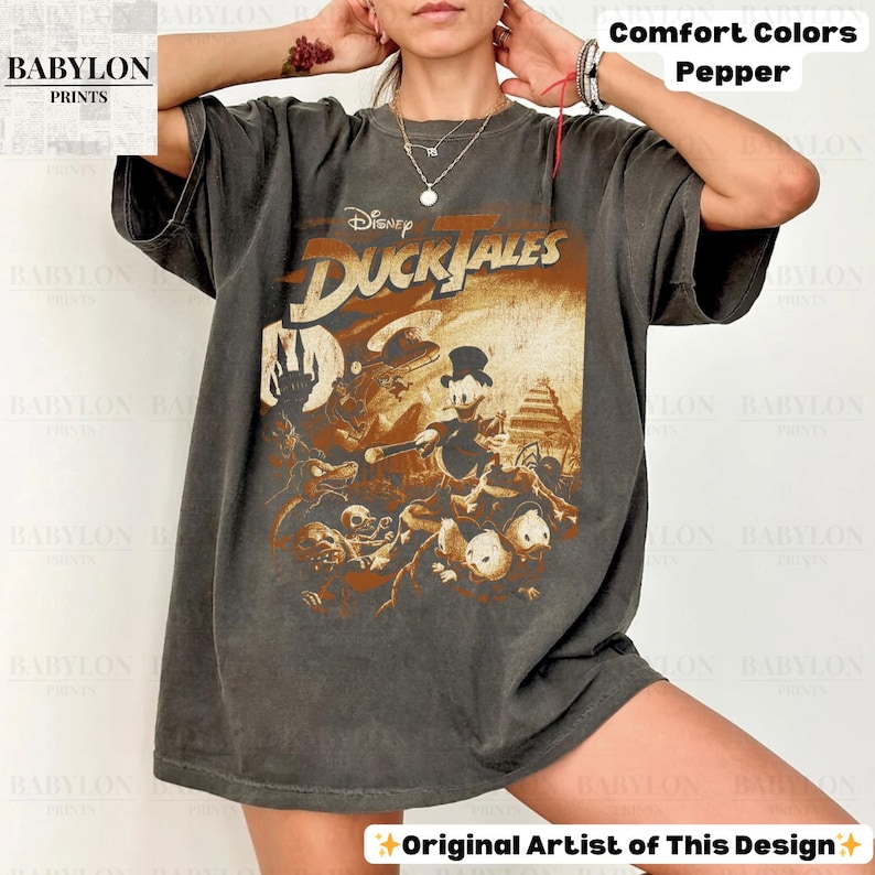 May include: Dark grey t-shirt featuring a vintage-style Disney DuckTales graphic. The design includes Donald Duck and other characters in a sepia-toned illustration. The shirt has the text "Comfort Colors Pepper" and "Original Artist of This Design".