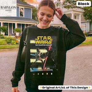 Puede incluir: Sudadera negra de Star Wars: La Amenaza Fantasma. El gr&aacute;fico presenta una escena con dos personajes empu&ntilde;ando sables de luz. La sudadera tiene el texto "STAR WARS THE PHANTOM MENACE" en amarillo y blanco. El logotipo de Babylon Prints est&aacute; en la esquina superior izquierda.