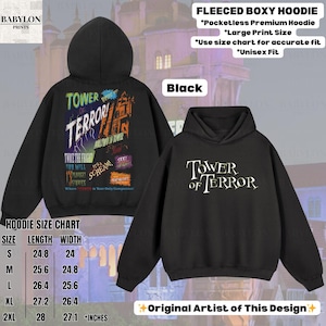 Op de afbeelding: Zwarte fleece boxy hoodie met "Tower of Terror" tekst op de voor- en achterkant. De achterkant heeft een kleurrijke afbeelding met de tekst "Tower of Terror" en andere zinnen. De maattabel van de hoodie is inbegrepen.