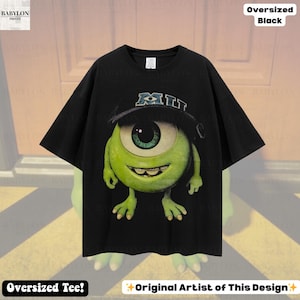 K&ouml;nnte beinhalten: Schwarzes, &uuml;bergro&szlig;es T-Shirt mit einer Grafik von Mike Wazowski aus Monsters, Inc., der einen Hut mit der Aufschrift "MI" tr&auml;gt. Das T-Shirt tr&auml;gt die Aufschriften "Oversized Tee!" und "Original Artist of This Design".