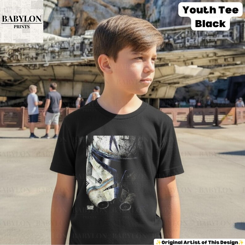 May include: A black short-sleeved t-shirt featuring a graphic print of a weathered white and blue clone trooper helmet on the front. The shirt has a crew neckline and is labeled as a Youth Tee Black. The design shows detailed battle-worn markings.