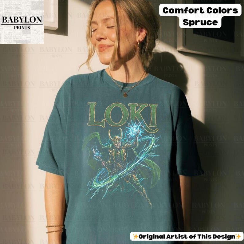 May include: Spruce-colored t-shirt featuring the word "LOKI" in green block letters above a graphic of a character with a horned helmet, holding blue energy. The shirt has short sleeves and a relaxed fit. The text "Comfort Colors Spruce" is at the top right. The text "Original Artist of This Design" is at the bottom.