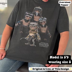 May include: A charcoal gray oversized t-shirt featuring a graphic print of four Ewok characters from Star Wars. The design includes the Star Wars logo in white text. The shirt has short sleeves and a crew neckline, presented in a relaxed fit.