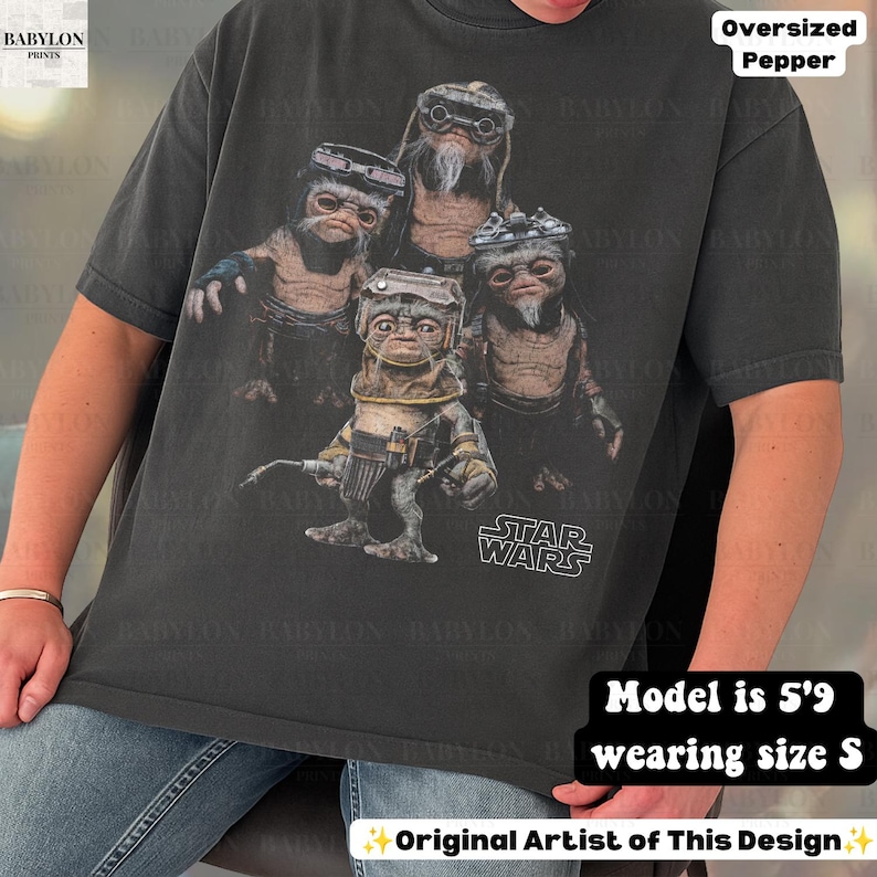 May include: A charcoal gray oversized t-shirt featuring a graphic print of four Ewok characters from Star Wars. The design includes the Star Wars logo in white text. The shirt has short sleeves and a crew neckline, presented in a relaxed fit.