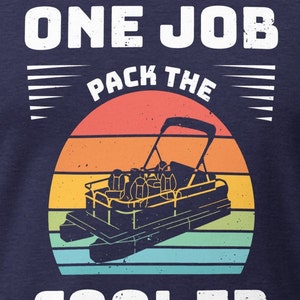 May include: A navy blue t-shirt with a white graphic design that says "You have one job pack the cooler". The graphic features a retro sunset with a pontoon boat in the center.