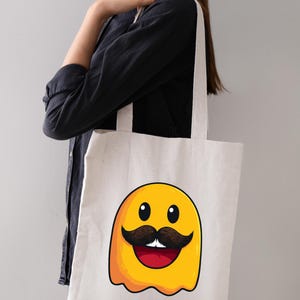以下が含まれることがあります： クリーム色のトートバッグ。黄色い体、茶色の口ひげ、黒い目、赤い口をした漫画の幽霊のデザインが特徴です。白いストラップが付いています。