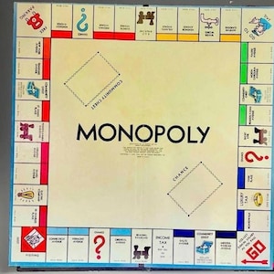 May include: A square Monopoly board game featuring a central cream-colored area with the word Monopoly printed in black. The perimeter consists of colored property spaces, railroads, utilities, and corner squares including Go, Jail, Free Parking, and Go to Jail.
