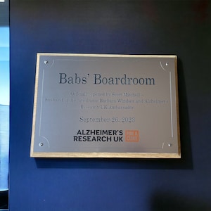 May include: A silver plaque with a wooden frame reads "Babs' Boardroom" and "Officially opened by Scott Mitchell - husband of the late Dame Barbara Windsor and Alzheimer's Research UK Ambassador. September 26, 2023" with the Alzheimer's Research UK logo below.
