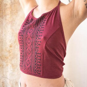 Pode incluir: Um top halter vinho com um padrão geométrico preto. O top é curto e tem um fecho de nó nas costas.
