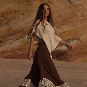 May include: A beige short-sleeved top paired with wide-leg brown trousers featuring a white geometric pattern along the hem. The trousers have a flared silhouette and a fringed edge detail at the bottom, creating a flowing appearance.