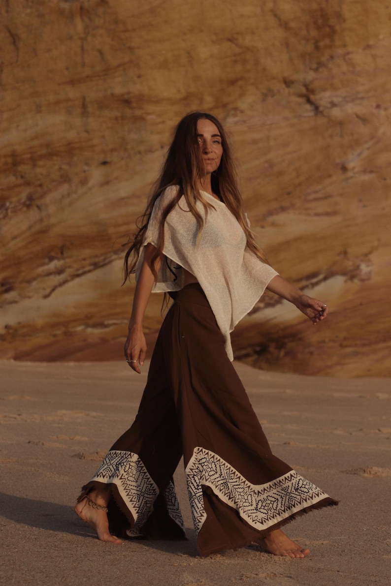 May include: A beige short-sleeved top paired with wide-leg brown trousers featuring a white geometric pattern along the hem. The trousers have a flared silhouette and a fringed edge detail at the bottom, creating a flowing appearance.
