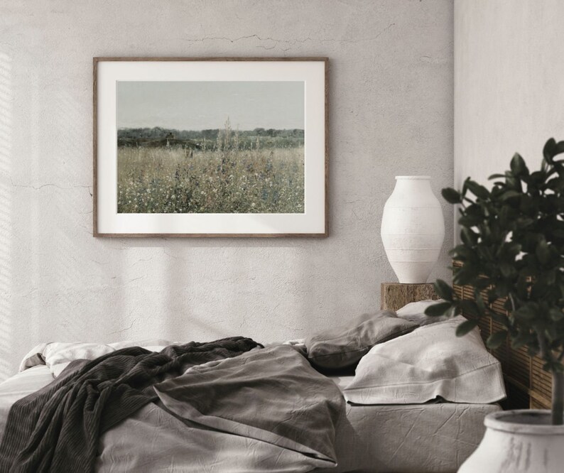 Puede incluir: Un interior de dormitorio con una cama con ropa de cama gris y negra, una fotograf&iacute;a de paisaje enmarcada en la pared, un jarr&oacute;n de cer&aacute;mica blanco sobre una mesa de madera y una planta en maceta en la esquina.